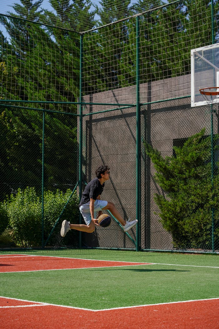 Energetic young man performing a jump shot on an outdoor basketball court.