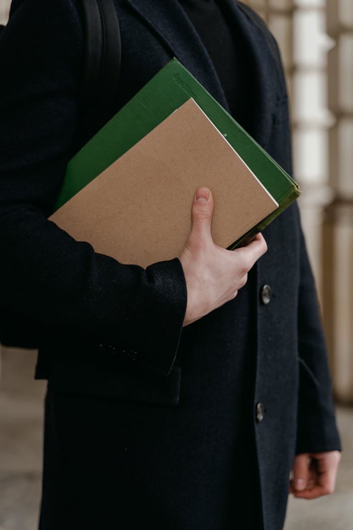 Close-up of an adult holding folders in a suit jacket, indoors, academic setting.